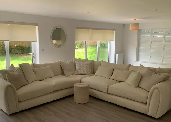 Living room with floor-length windows to a garden, white blackout roller blinds, and white shutter blinds on side window.